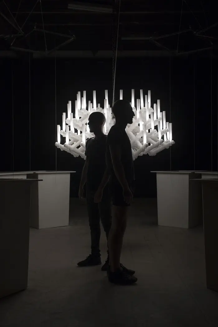 Zwei Schattengestalten in einem dunklen Raum vor einem hellen Kronleuchter