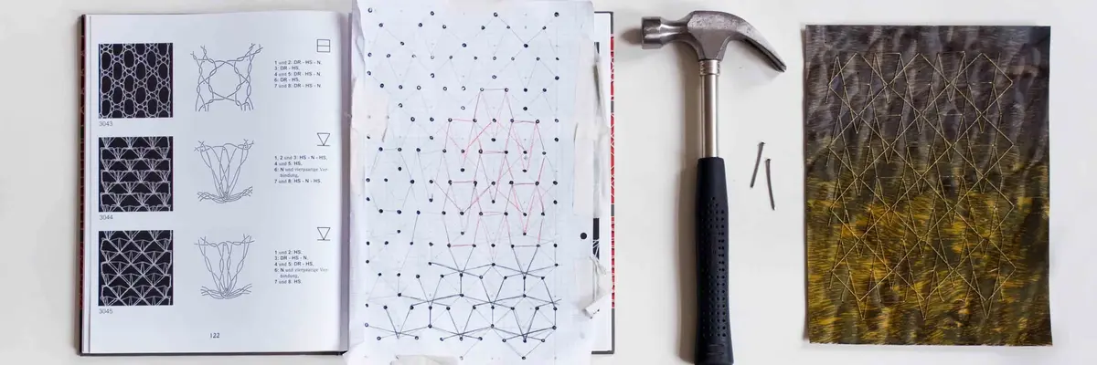 Buch mit Häkelanleitungen, daneben Skizze, Hammer, Nägel und eine Art besticktes Textil