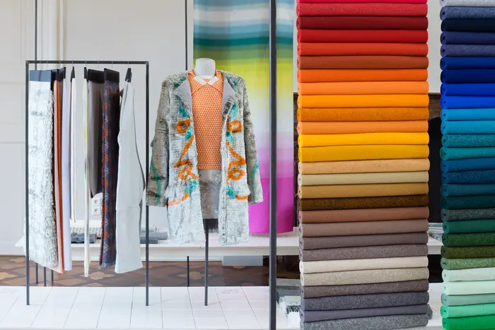 Kleidung an Kleiderstangen, daneben viele gestapelte Stoffrollen