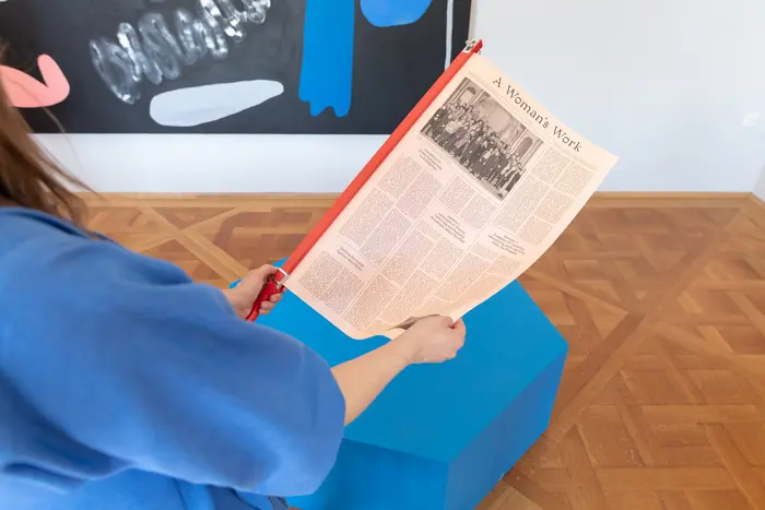 Ausstellungsansicht mit einer Frau, die Zeitung liest 