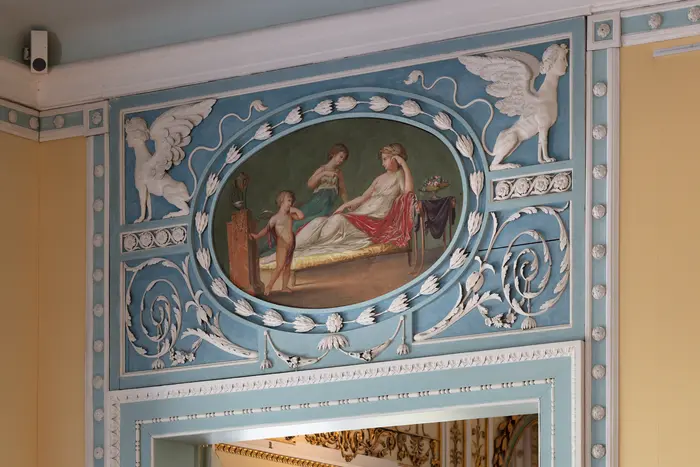 Weiße schwungvolle Stuckverzierungen um ein Gemälde einer Frau mit zwei Kindern 