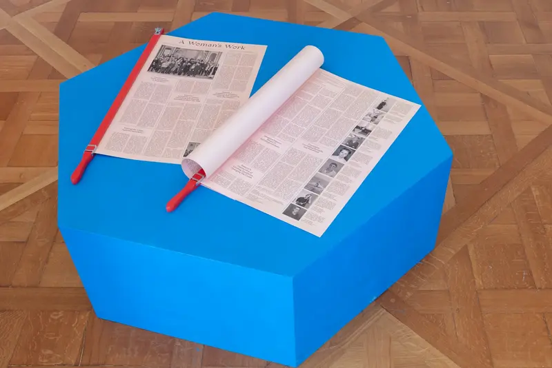 Ausstellungsansicht eines blauen Hockers auf dem zwei Zeitungen ausliegen