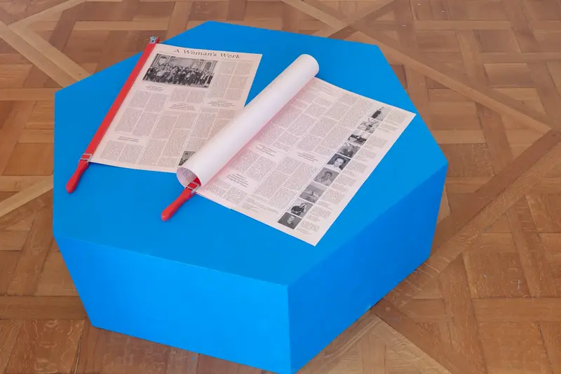 Ausstellungsansicht eines blauen Hockers auf dem zwei Zeitungen ausliegen