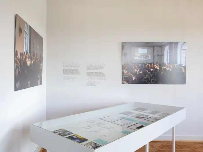 Ausstellungsansicht mit zwei Fotos und einem Schaukasten mit Dokumenten